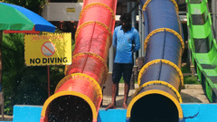 A set of vibrant, twisting water slides at Black Thunder Water Theme Park, with a rider splashing into the pool while a lifeguard stands by.
