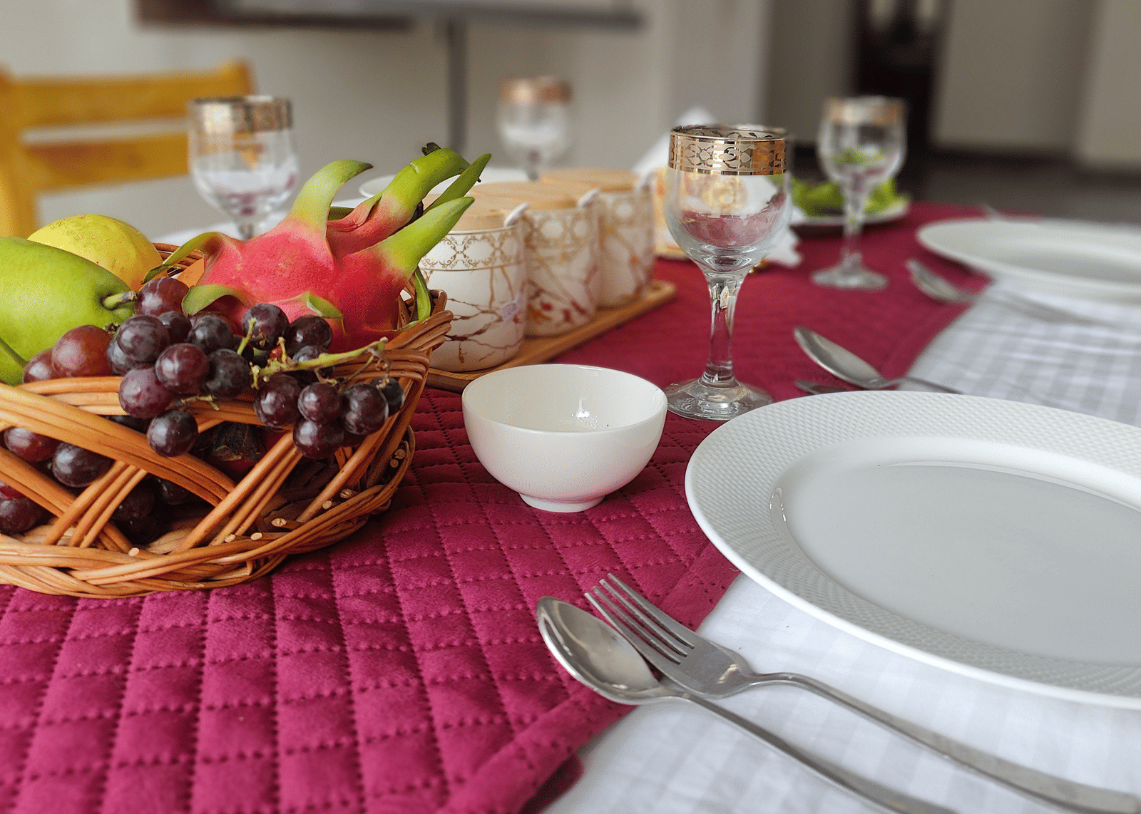 A close-up of a dinner table set with a red runner, white plates, and a basket of fresh fruit at Indus Serenity Retreat.