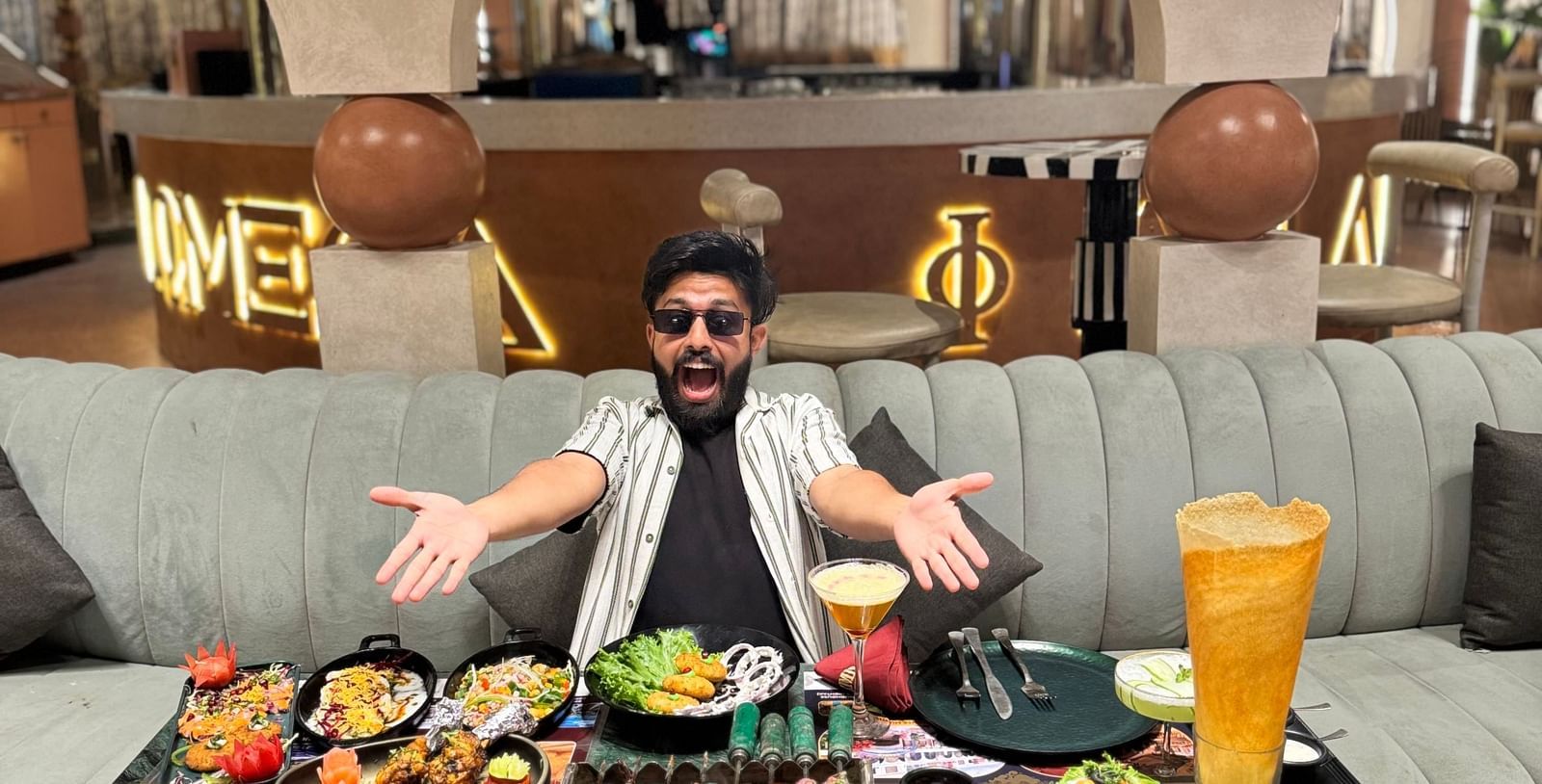 A person at a table at Themis Barbecue House, Ambala, with a variety of colorful food dishes and drinks spread out.