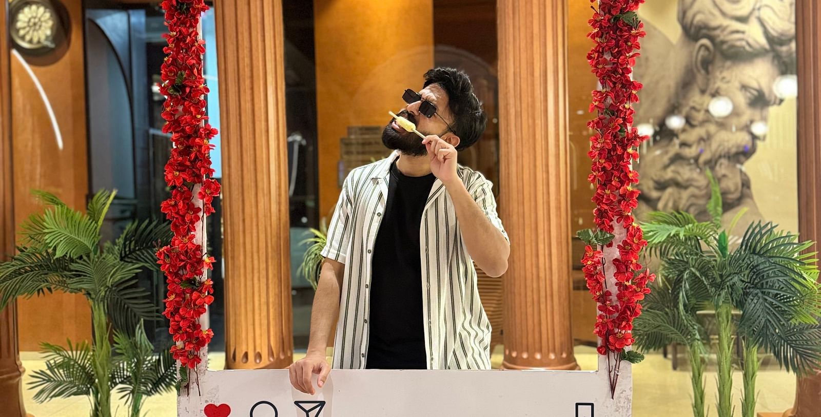 A person posing inside a decorated photo booth at Themis Barbecue House, Ambala, featuring flowers and social media icons.