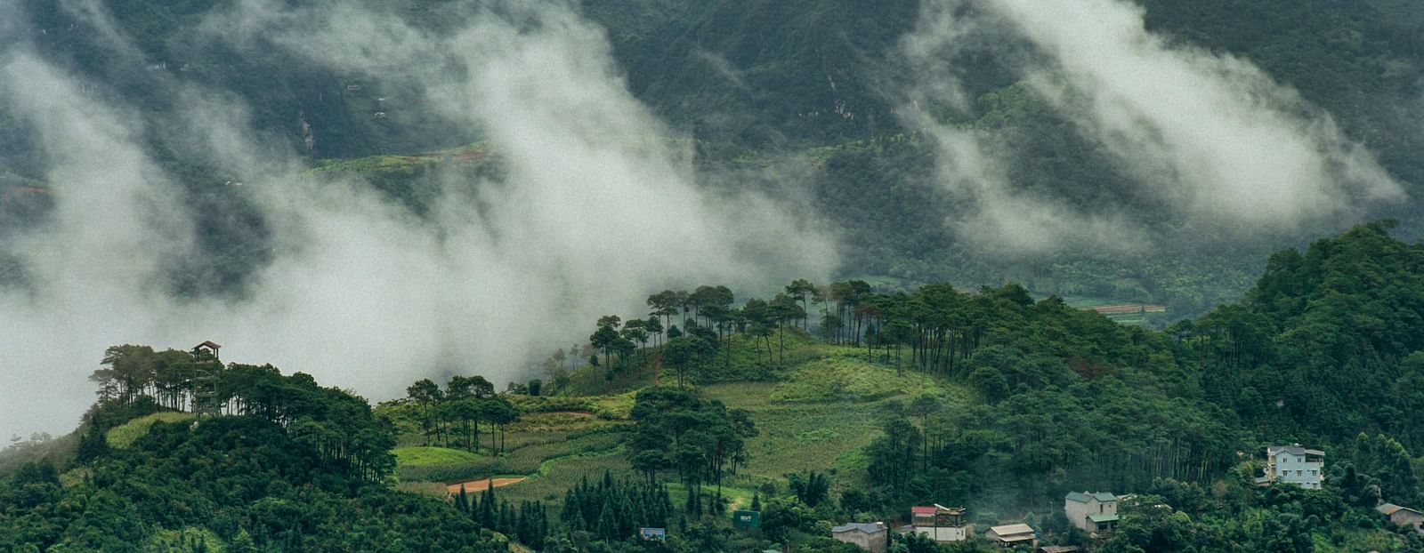 An aerial view of a village next to a mountain with mist flowing into the village