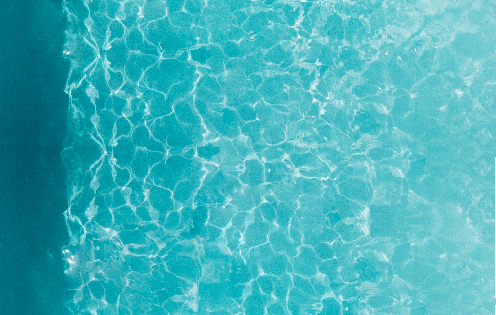 An overhead shot of a person swimming in a clear, turquoise outdoor swimming pool.