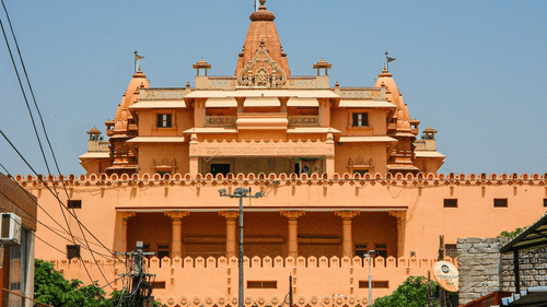 A multi-tiered, peach-coloured Hindu temple complex standing tall under a clear blue sky.