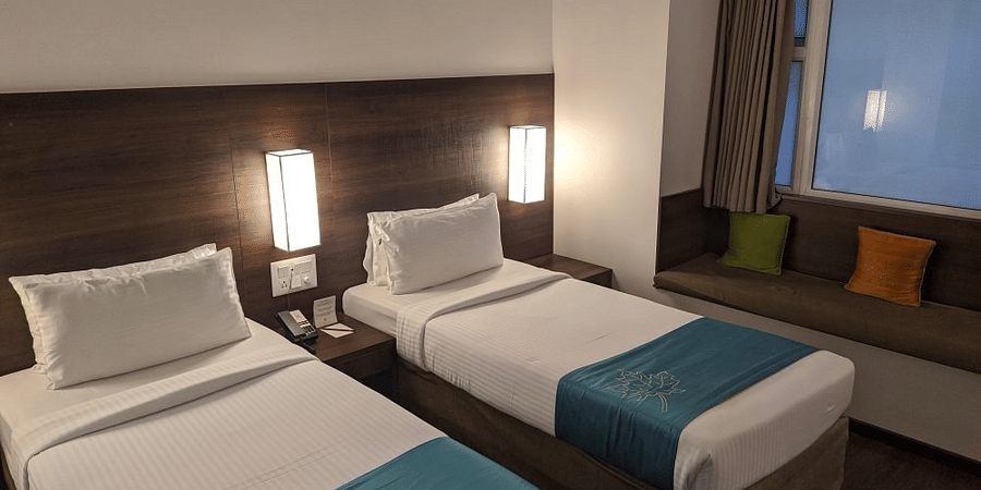 The Comfort Room at Temple Tree Hotel, Bangalore showcasing twin beds, a wooden head board, overhead lamps, and a large glass window.