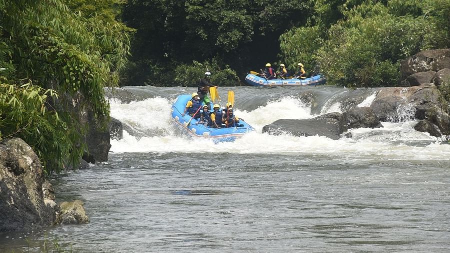 A group of people in blue rafts navigating through white water rapids, surrounded by lush greenery - Evergreen County