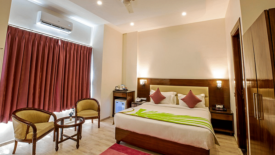 The Deluxe room with a double bed along with two cushioned arm chairs kept in front of the window covered by curtains at Regenta Inn DLS.