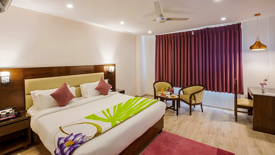 A wide angle shot of the Premium Room with a red carpet in front of the double bed along with a work station in the corner of Regenta Inn DLS.