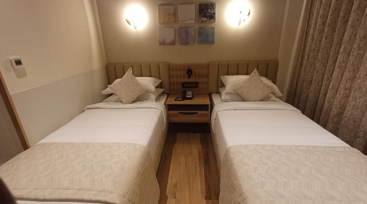 Image of a room with twin beds and a lights above the bed  at Hotel Raai, Hosur.