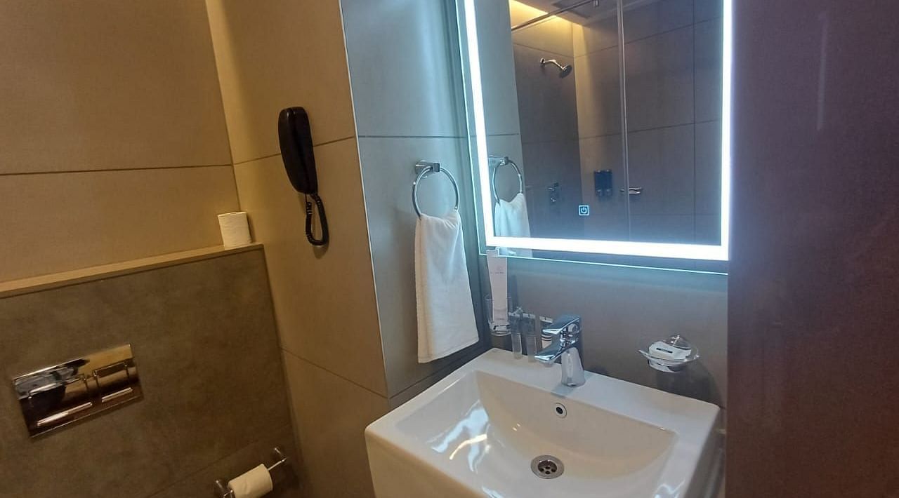 Image of a restroom wiith sink and lighted mirror at Hotel Raai, Hosur.