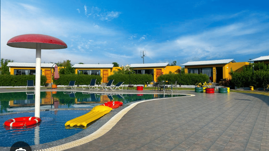 A serene swimming pool area is featured, complete with vibrant loungers under a bright and cloudless summer sky.