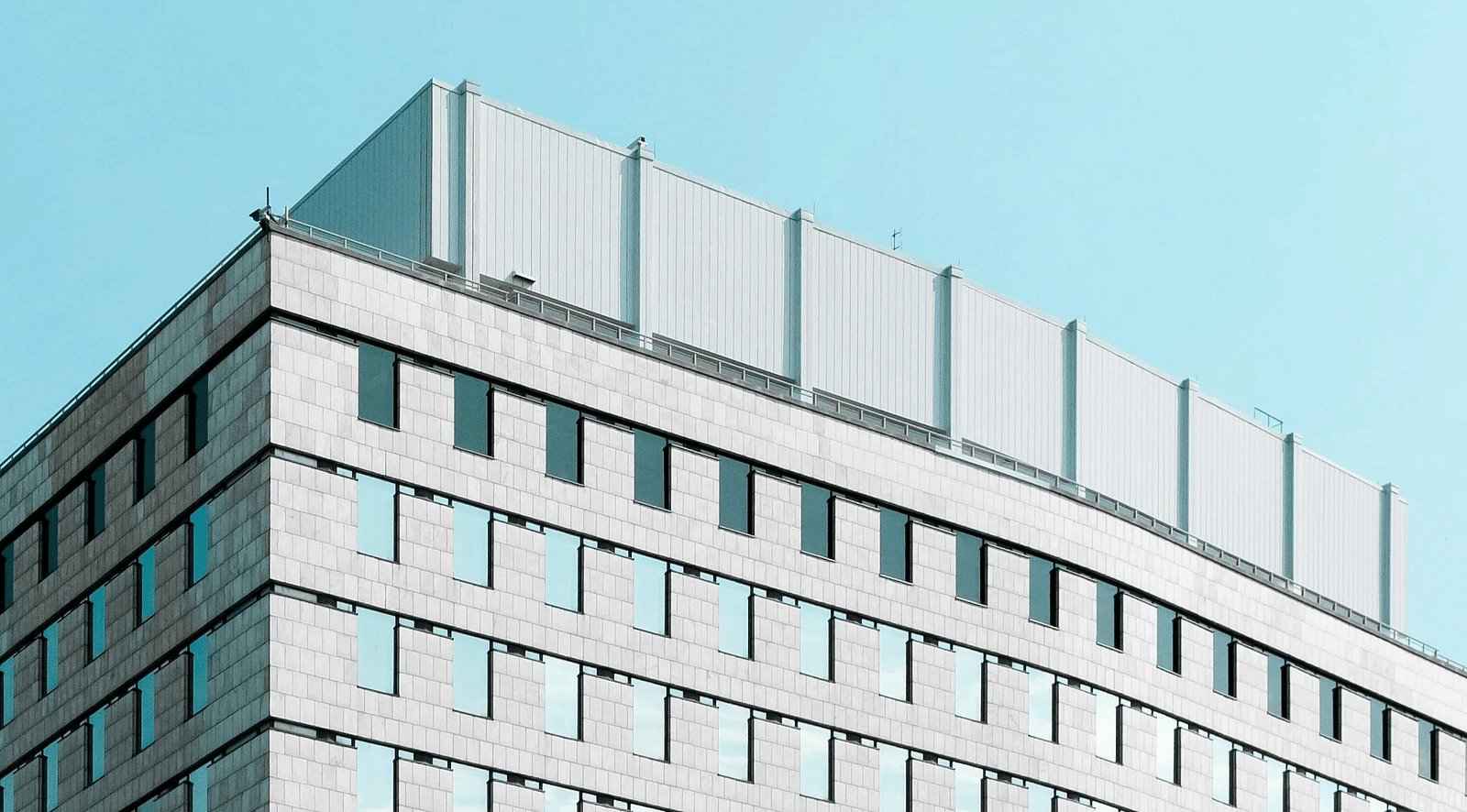 A tall modern building with a repeating pattern of windows against a bright sky.