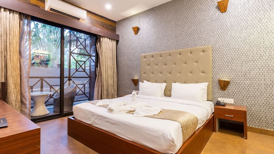 Premium Room at Amara Oceanfront Resort, Baga with a queen size bed, tufted headboard, bedside tables, patterned wall, and balcony seating visible outside.