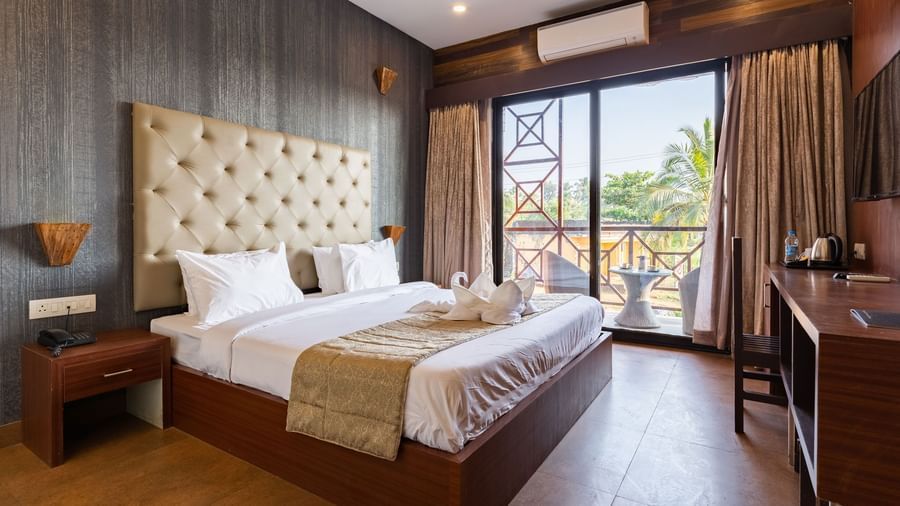 Premium Room at Amara Oceanfront Resort, Baga with a large bed, tufted headboard, desk, bedside table, and balcony seating with outdoor view.