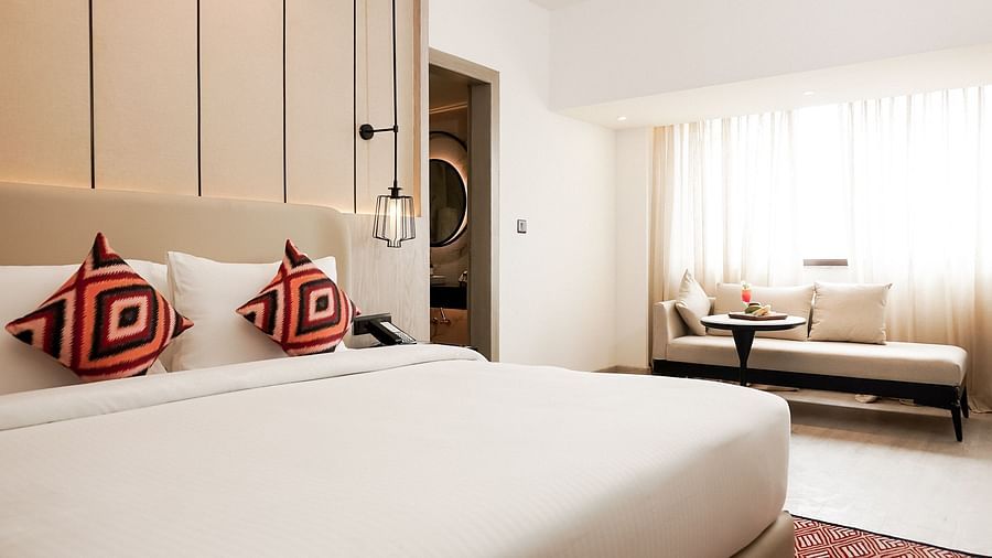 Bright hotel room with a plush double bed, red patterned cushions, pendant lights, and a cosy seating area by the window with a table set for snacks and drinks - Golden Tulip, Lucknow