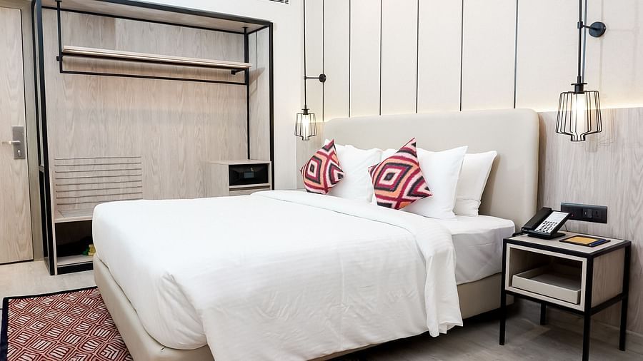 Stylish hotel room with a double bed, white linens, patterned red cushions, pendant lights, open wardrobe with shelf and safe, and a bedside table with a phone - Golden Tulip, Lucknow