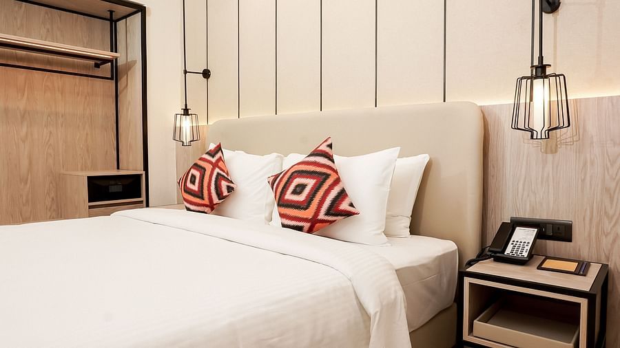 Modern hotel room with a double bed, white linens, red patterned pillows, pendant lights, bedside table with phone, and an open wooden wardrobe - Golden Tulip, Lucknow