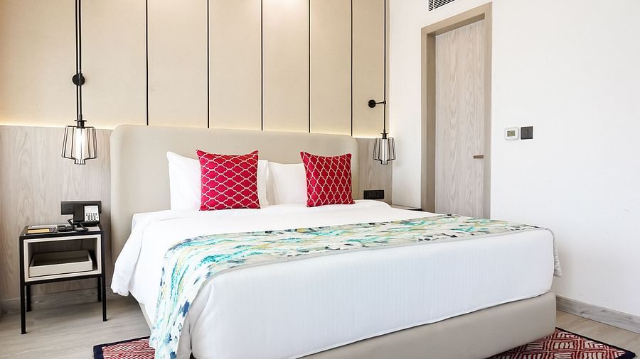 Contemporary hotel room with a king size bed, white bedding, red accent pillows, pendant lights, a bedside table with a phone, and a patterned rug - Golden Tulip, Lucknow