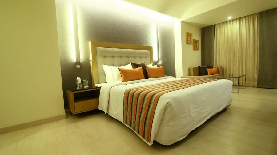 Spacious well lit bedroom at the Sonnet, Jamshedpur with a king bed, side table and curtained windows.