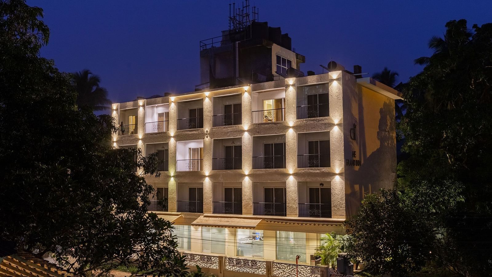 Facade of Calux Grand Inn, Calangute with trees on the sides with a clear sky in the background.