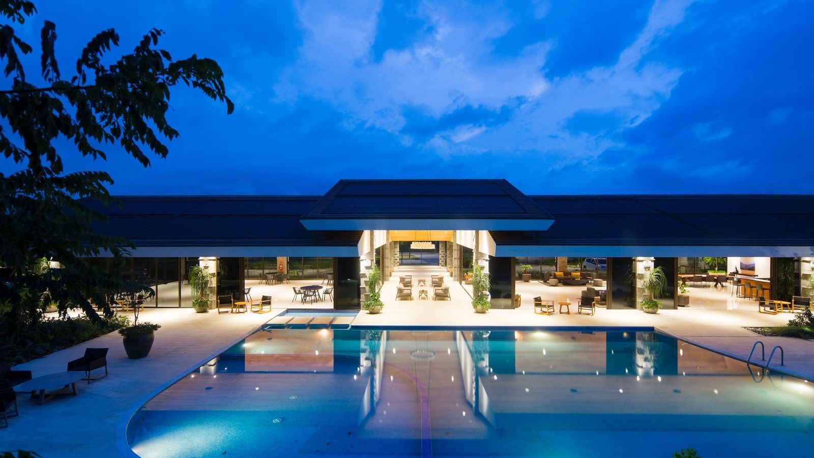 facade image of a property with a vast swimming pool in the foreground on a late evening