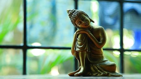 A Buddha figurine with him sitting with one leg raised, hands resting on the knee, and his head gently leaning on his hands