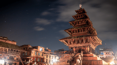 Dramatic night view of the illuminated five-story Nyatapola Temple pagoda under a cloudy sky in Taumadhi Square, Bhaktapur, Nepal.