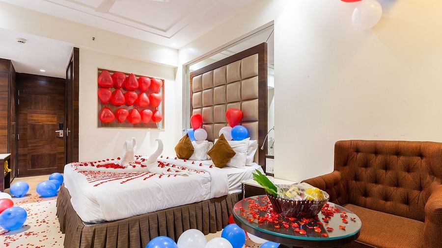 Image of a room with a sofa and a bed decorated with balloons and flower petals at Calux Grand Inn, Calangute.