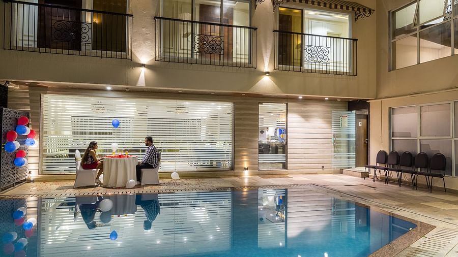 Image of two people dining beside a swimming pool at Calux Grand Inn, Calangute.