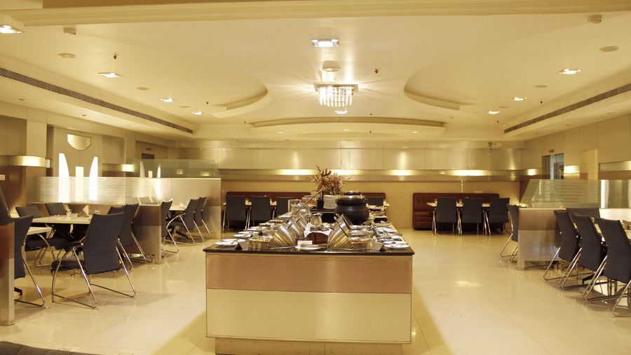 The restaurant at DSF Grand Plaza, Tuticorin with a central buffet counter of chafing dishes, dining tables with dark chairs, and a chandelier overhead.