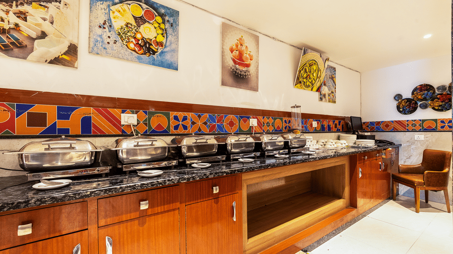 A buffet counter at The Curry House displaying a selection of food in chafing dishes, complete with vibrant food photography and colourful tiled wall patterns at Hotel Corporate Suites