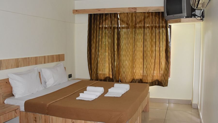 A side view of the room at Riverside Inn with a large bed beside a window covered with curtains, and a wall-mounted AC and TV next to it.