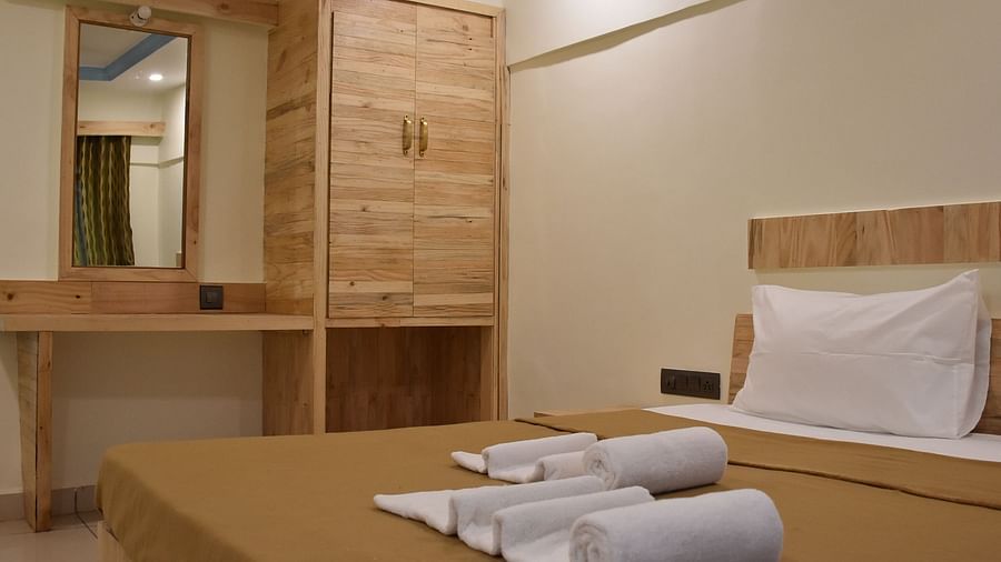 A close-up view of a bed at Riverside Inn with rolled towels placed on it, alongside a wooden wardrobe and a desk with a wall-mounted mirror.