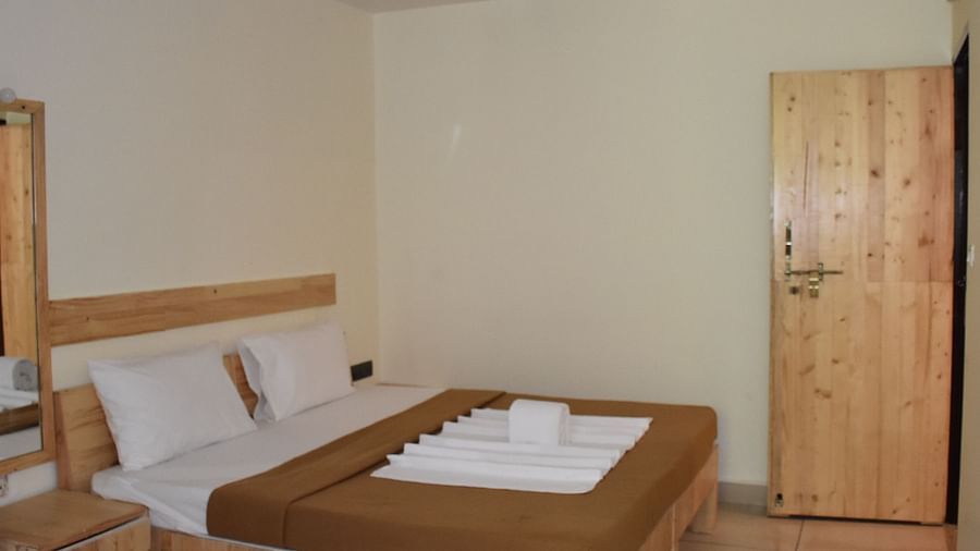 A side view of a neatly made bed at Riverside Inn, featuring arranged pillows, curtains, and neatly placed towels.