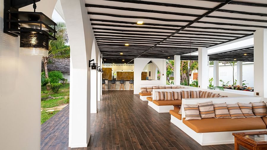 Open-air lounge with long cushioned benches, wooden floors, and garden views through arched openings - Shooting Star Boutique Hotel.