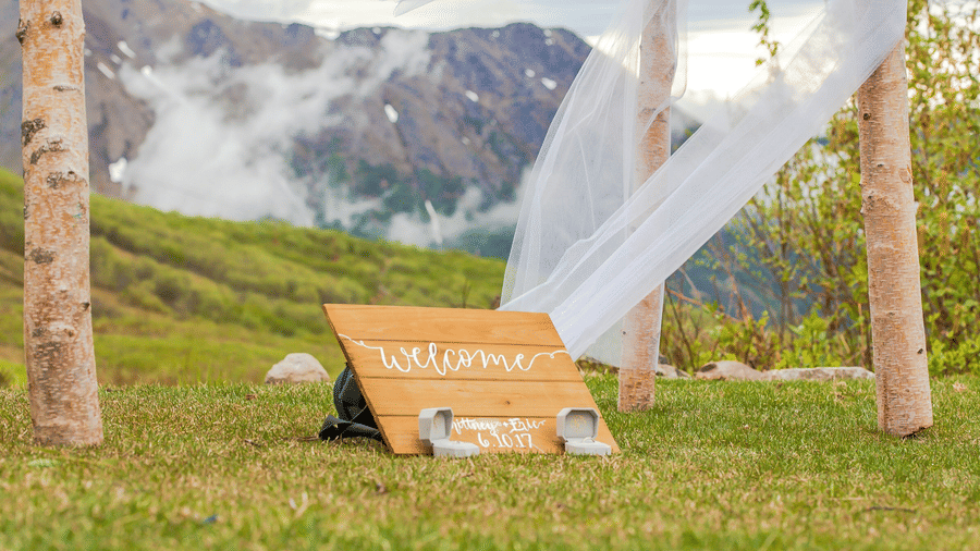 A wooden board with the words welcome and two ring boxes placed below it