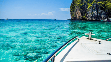 View from a boat moving across clear blue sea toward rocky cliffs.