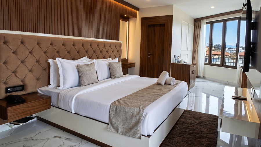 A Junior Suite AC Room at Valmere Chery Blossom Suites featuring a plush bed with a big headboard, a nightstand, and tiled flooring.