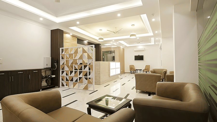 The lobby lounge at Hotel Apple Park Delhi featuring tan leather armchairs, a glass coffee table, and a white decorative partition wall under recessed ceiling lights.