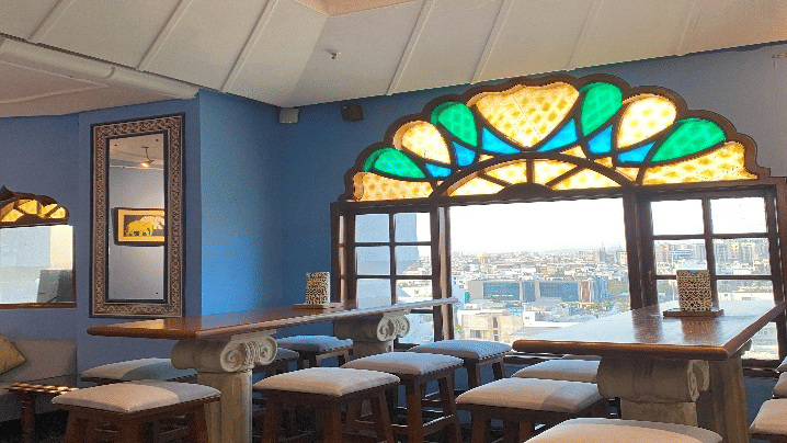 Dining area with large windows and colourful stained-glass decor at Clarks Amer, Jaipur.