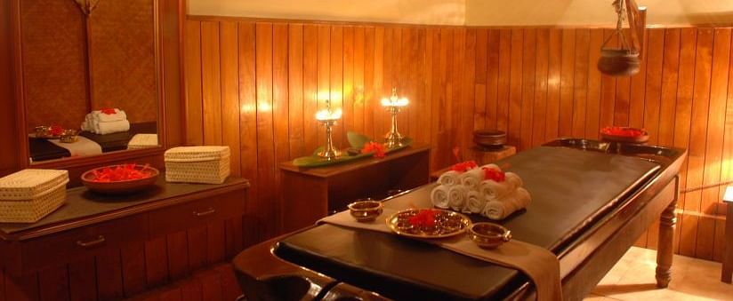 Warmly lit spa treatment room with a massage table and various wellness products - BluSalzz Collection - Tranquil Resort, Wayanad