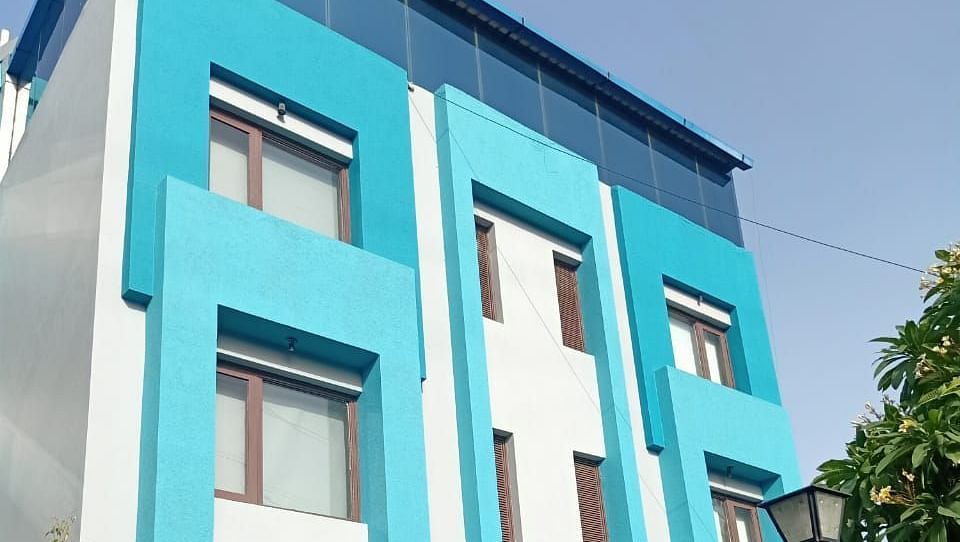 A colourful blue building with multiple windows and some greenery in front - Asian Suites IFFCO Metro, Gurgaon