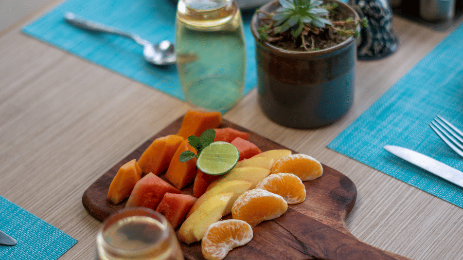 A table setting at BluSalzz Escapade Resort, Lansdowne, displays a platter of fruit slices, a glass of water, cutlery, and place mats.