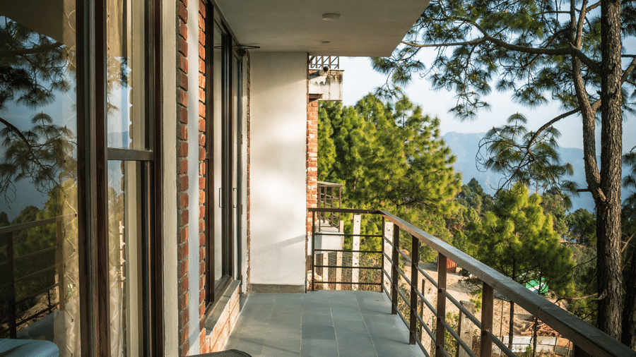 A balcony features a chair and a railing outside the Pine Forest Suite. Trees and hills are visible beyond the structure.