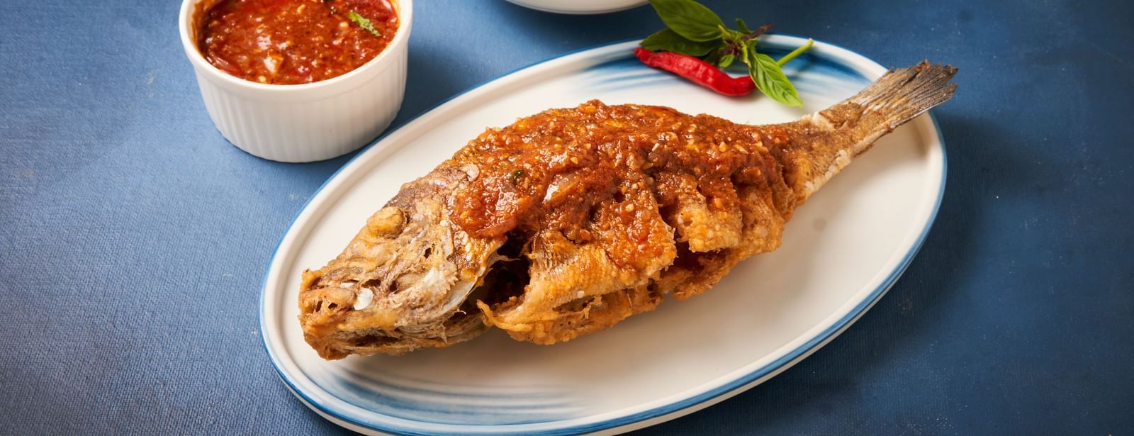 A whole fried fish on a plate with chutney and a bowl of rice at Grande Bay Resort & Spa.