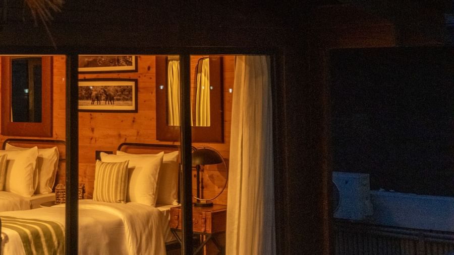 Cosy wooden cottage bedroom warmly lit with twin beds and rustic decor at Rhino and River BluSalzz Collection, Pobitora.