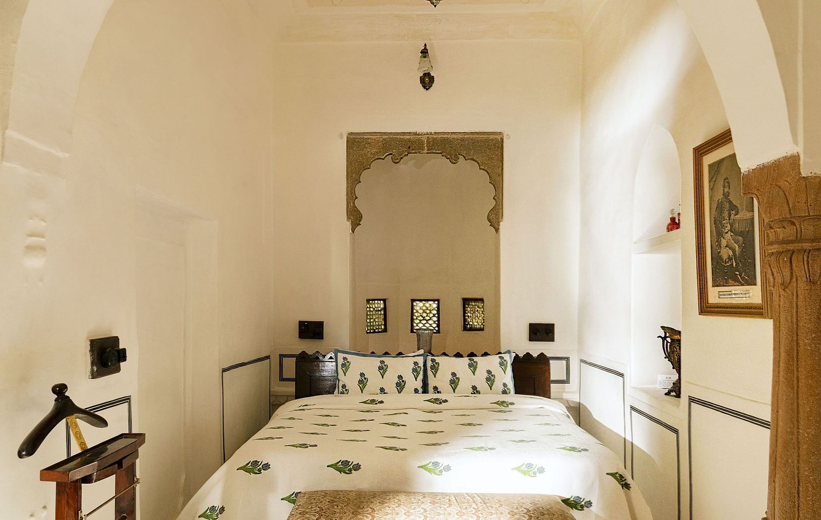 A bright bedroom at Fort Barli, featuring a white arched doorway and a patterned bed, offers a minimalist yet elegant sleeping space.