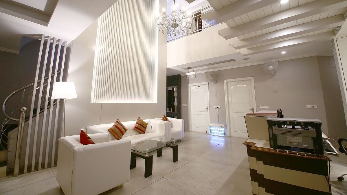 A hotel lobby with a white sofa, decorative pillows, a textured wall with lighting, a spiral staircase, and a reception desk, lit by a chandelier. - Hotel Diamond Plaza, Chandigarh.
