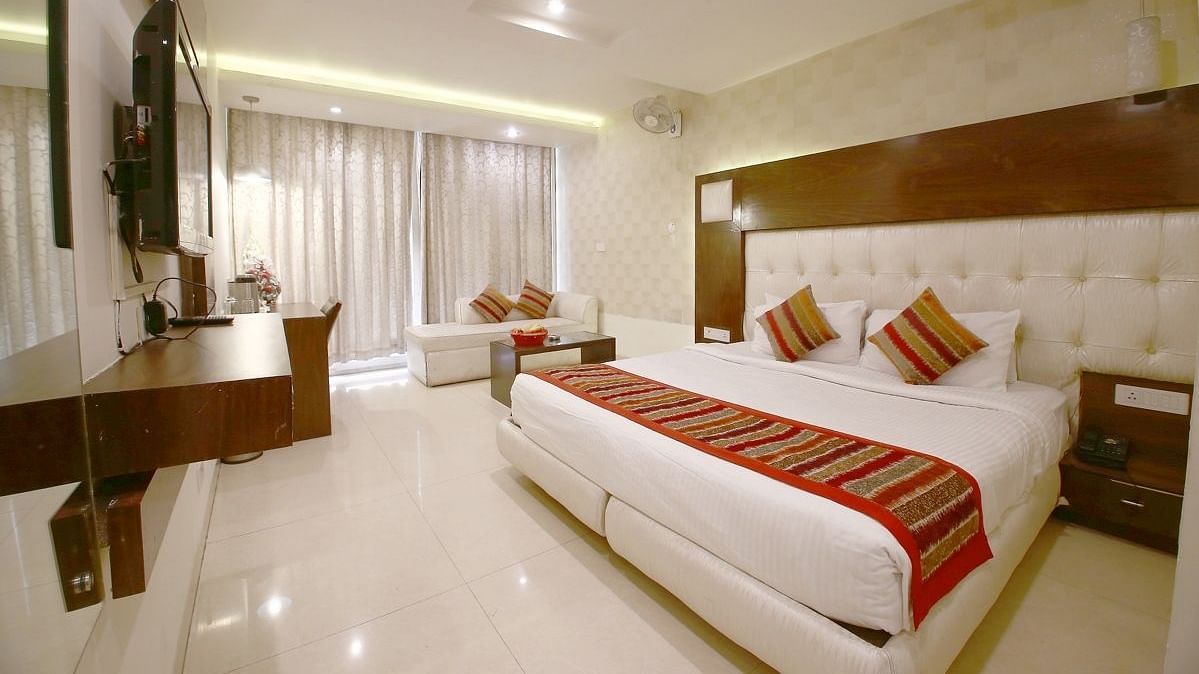 A well-lit, spacious hotel room with a plush bed featuring decorative pillows and a runner, a sofa, and a desk, creating a welcoming atmosphere. - Hotel Diamond Plaza, Chandigarh.