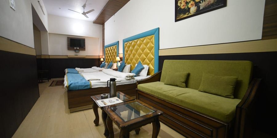 Four bed deluxe room with sofa and table on the side at Hotel Panchvati Inn, Joshimath