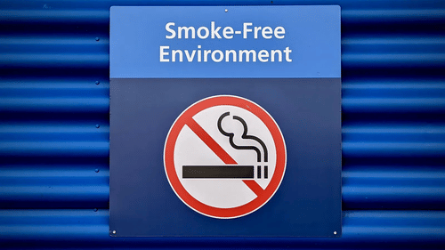 A blue square sign reading 'Smoke-Free Environment' with a no-smoking symbol is mounted on a corrugated blue wall.